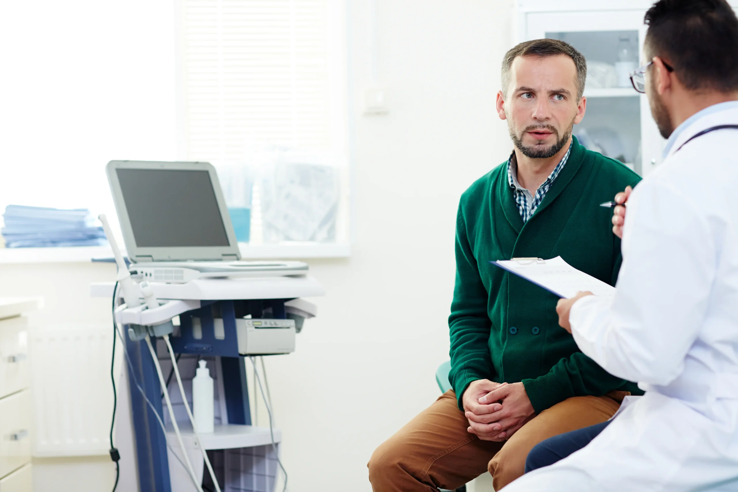 Doctor discussing hemorrhoid bleeding and colon cancer screening with a male patient in an exam room